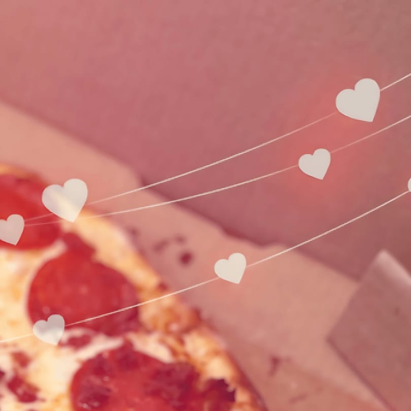 Pepperoni pizza in a box with white heart decorations on strings, conveying love for pizza.