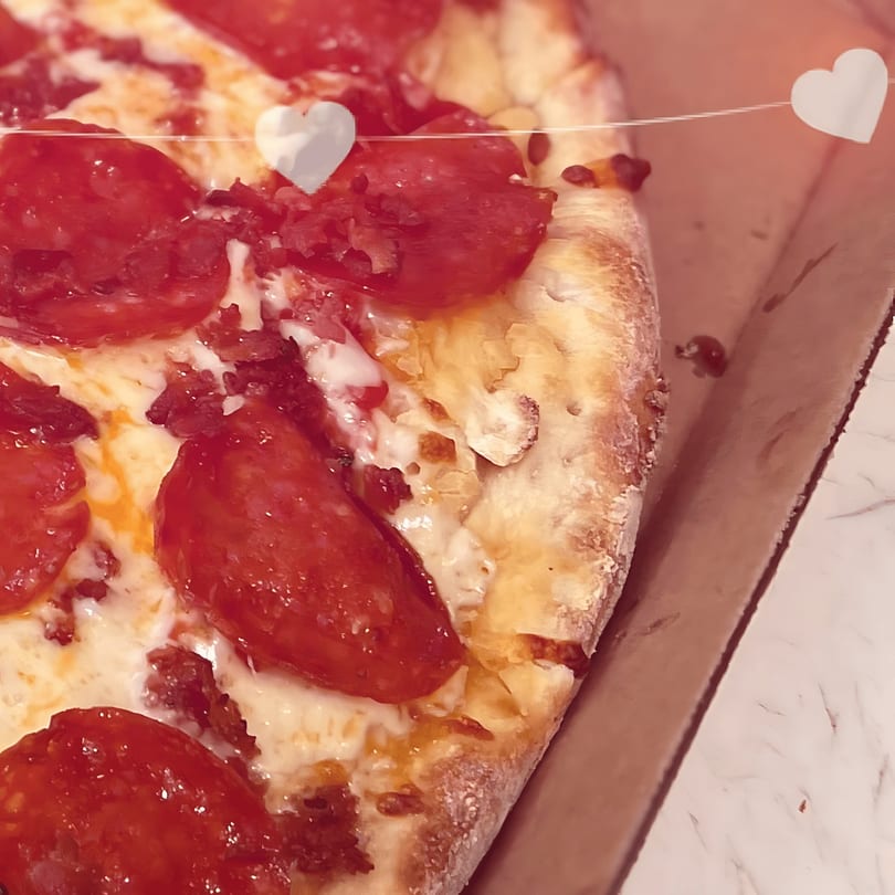 Close-up of a pepperoni pizza with melted cheese and a thick crust, with heart decorations.
