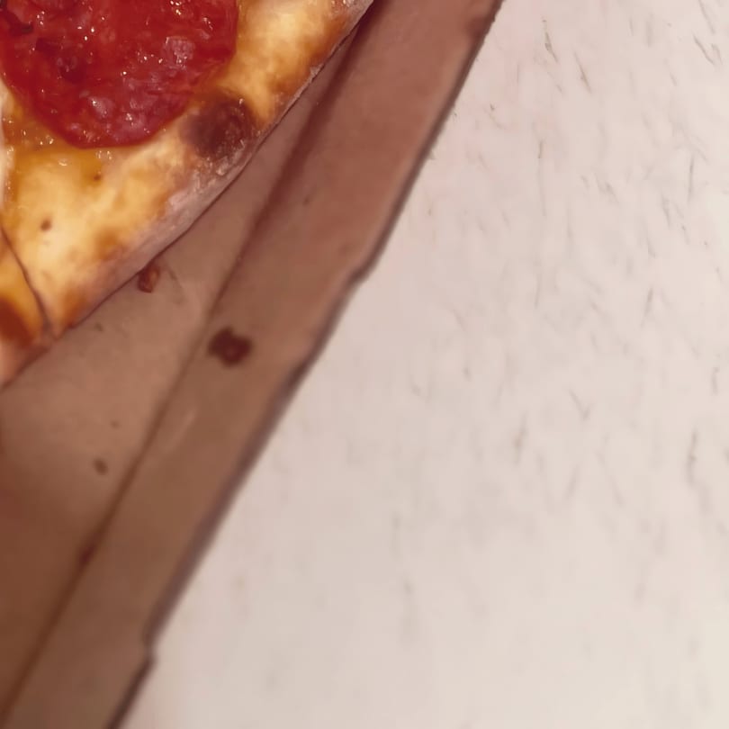 A close-up of a pepperoni pizza slice with melted cheese in a cardboard box.