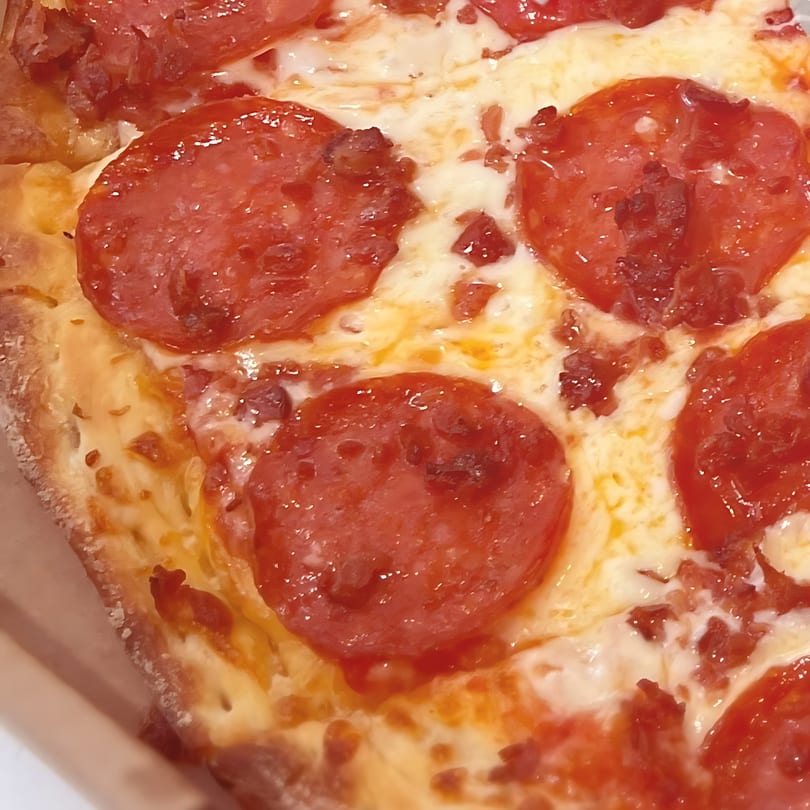 Close-up of a North Beach Pizza pepperoni slice with melted cheese and crispy crust.