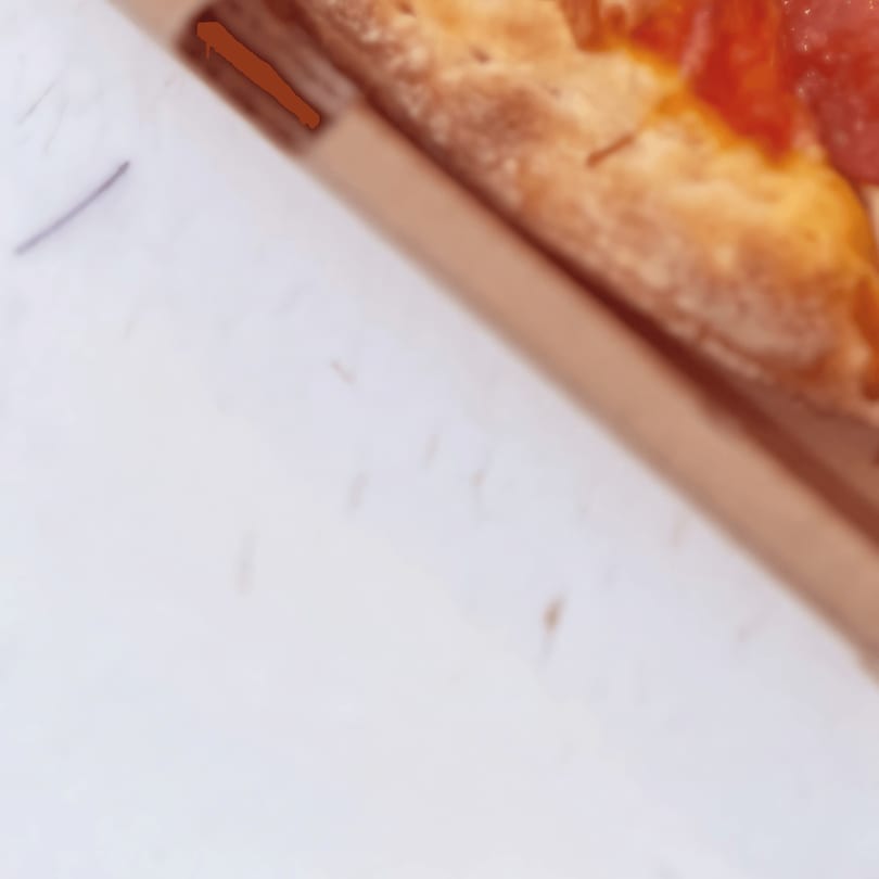 A close-up, top-down view of a pepperoni pizza slice in a cardboard box.