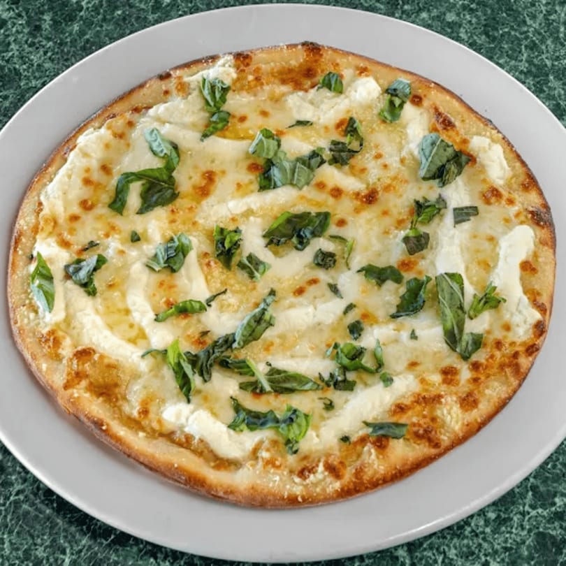 North Beach Pizza's white pizza with melted cheese, ricotta, and fresh basil on a white plate.
