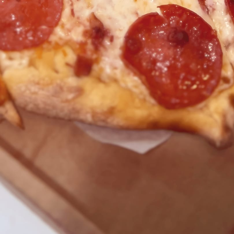 Close-up of a slice of North Beach Pizza pepperoni pizza in a brown box.