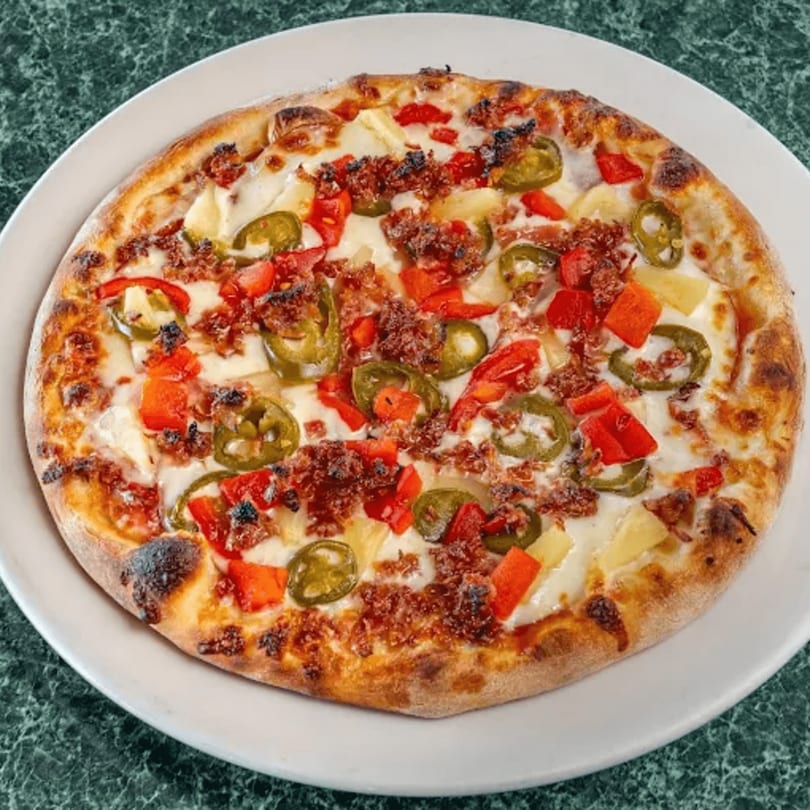 North Beach Pizza with sausage, red peppers, jalapeños, and pineapple on a white plate.
