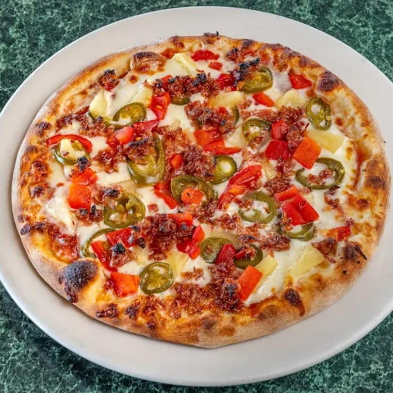 A North Beach Pizza with red peppers, pineapple, jalapeños, and crumbled sausage on a white plate.