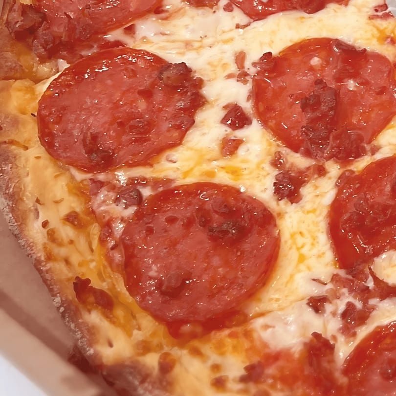 Close-up of a North Beach Pizza pepperoni pizza slice with melted cheese and crispy crust.