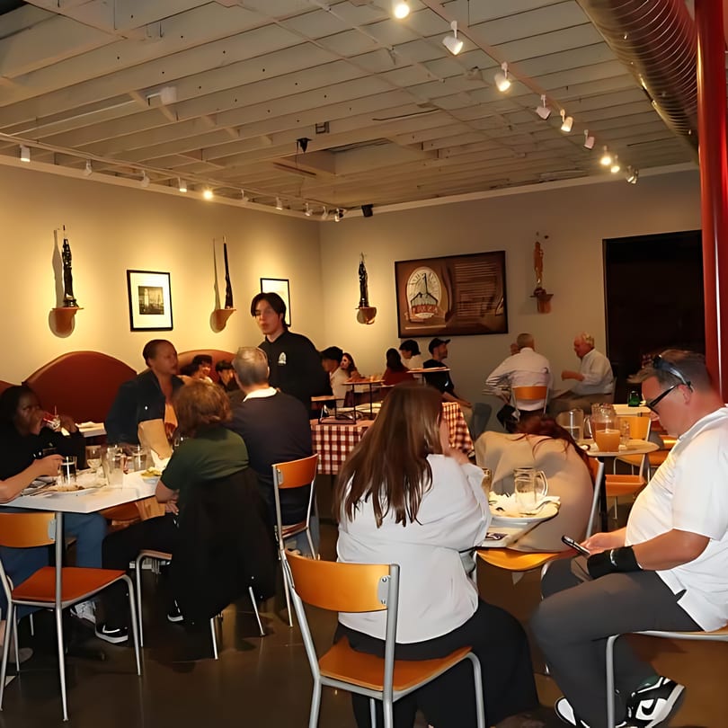 A busy North Beach Pizza dining room with patrons seated at tables and a server attending to them.