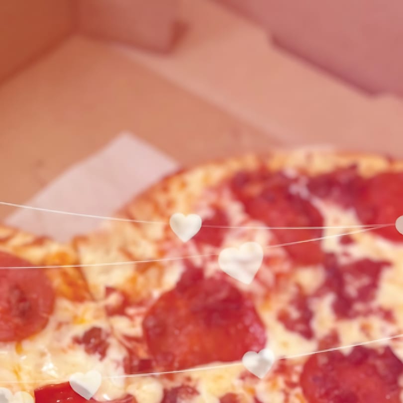 Pepperoni pizza in a box, with white heart decorations strung across the foreground.